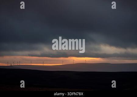 West Yorkshire, Regno Unito. 13 gennaio 2026. Halifax, West Yorkshire, Regno Unito. Tempo Regno Unito il sole tramonta sopra la valle di Calder con la sagoma di turbine eoliche lontane sulla linea aerea e il profilo del monumento Stoodley Pike si trova in alto sulle brughiere Pennine sopra Hebden Bridge, West Yorkshire, Regno Unito . La fotografia è stata scattata da Ovenden Moor, Halifax, West Yorkshire. Crediti: Immagini di mulini a vento/Alamy Live News Foto Stock