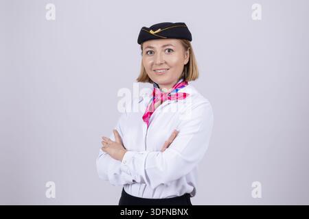 Assistente di volo sorridente in uniforme formale in piedi con le armi incrociate Foto Stock