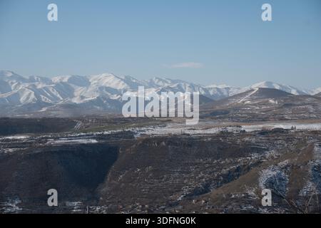 La catena montuosa innevata in Armenia si estende su colline ondulate, profonde valli sotto il cielo azzurro, con tonalità fresche e un'atmosfera invernale tranquilla Foto Stock