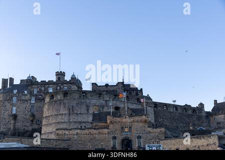Un castello di pietra con torri multiple, bandiere e merlature contro un cielo azzurro. Diversi uccelli volano in alto a Edimburgo, in Scozia. Foto Stock