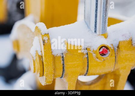 Connettore idraulico industriale giallo innevato con asta cromata e raccordo rosso, dettaglio macro di componenti per macchinari pesanti che mostrano condizioni climatiche fredde Foto Stock