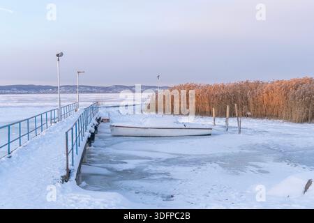 Molo ghiacciato e barca con canne sul lago ghiacciato in inverno, nel lago Balaton, Ungheria Foto Stock