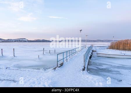 Molo ghiacciato e barca con canne sul lago ghiacciato in inverno, nel lago Balaton, Ungheria Foto Stock
