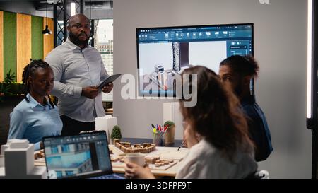 Ingegnere immobiliare afro-americano che presenta il piano di preparazione del sito e le normative sulla suddivisione in zone sui modelli 3D durante una sessione di collaborazione con il team. Iniziativa abitativa per la pianificazione urbana. Foto Stock