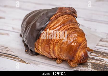 Un'intima scena di un caffè mattutino, dove un croissant solitario riposa su un piatto di porcellana accanto a una tazza per la cottura a vapore Foto Stock