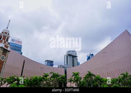 Uno scatto grandangolare basso che cattura l'iconica giustapposizione della Torre dell'orologio Tsim Sha Tsui di Hong Kong, la moderna architettura inclinata di Hong Kong Foto Stock