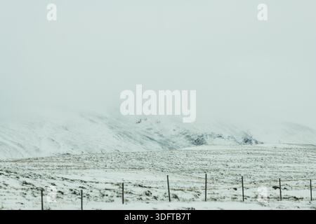 Vista di un paesaggio innevato sotto un cielo piatto e bianco, con una catena montuosa lontana sbiadita sullo sfondo, Hvitserkur, penisola di Vatnsnes, a nord Foto Stock
