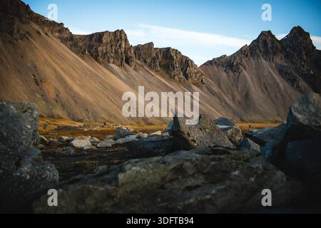 Vista delle montagne frastagliate e imponenti che si innalzano drammaticamente dalle pianure dorate e erbose sotto un cielo sereno, Vestahorn, Hofn, regione degli Eastfjords, Islanda. Foto Stock