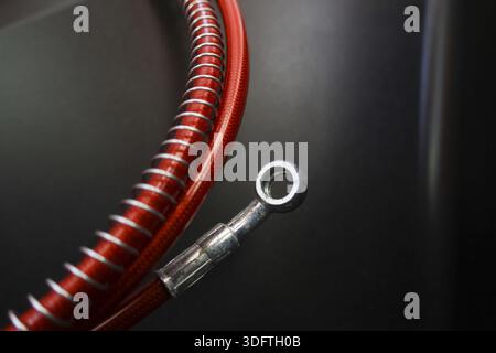 Tubo flessibile del freno per motociclette rosso intrecciato e raccordo banjo argento sfondo nero scuro che mostra resistenza durata potenza velocità e ingegneria di precisione per Foto Stock