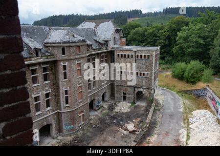 Vista dal tetto dell'esterno di un grande edificio vuoto e abbandonato, parzialmente demolito. Detriti a livello del suolo. Circondato dalla foresta. Foto Stock