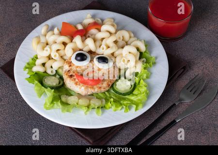 Cibo divertente per bambini - una ragazza sorridente di tacchino, cavatappi di pasta, olive, pepe, uovo e cetriolo su piatto bianco su sfondo marrone Foto Stock