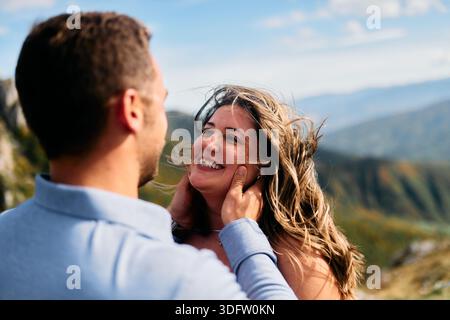 Uomo che tiene donne faccia in un gesto romantico contro un paesaggio di montagna Foto Stock