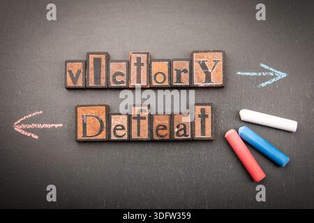 Parole di vittoria e sconfitta mostrate con blocchi di legno e frecce di gesso sulla superficie della lavagna Foto Stock
