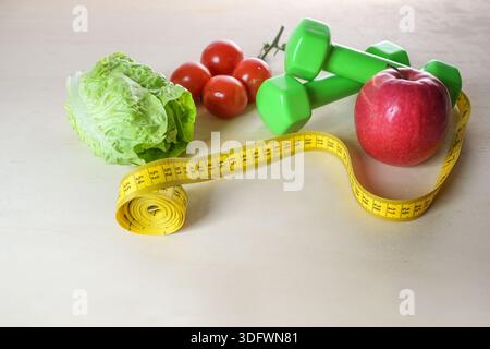 Mele, verdure, manubri e metro a nastro su uno sfondo di legno leggero, alimentazione sana e esercizio fisico per fitness, perdita di peso e salute, copia spac Foto Stock