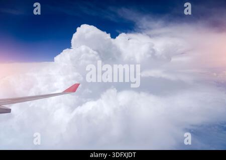 Splendida vista dalla finestra dell'aeroplano di un'ala sopra lo strato di nuvole sparsi del cumulus e il paesaggio montuoso. Viaggiare in aereo in alto sopra un limpido Foto Stock