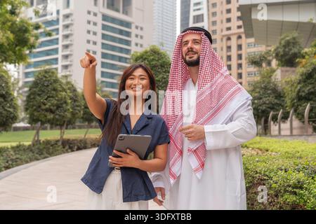 Due uomini d'affari asiatici e arabi lavorano insieme all'aperto in una città, discutendo idee e strategie per il business immobiliare. Foto Stock