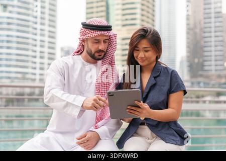 I professionisti del settore, il Medio Oriente e l'Asia discutono le idee utilizzando un tablet mentre si siedono in una città moderna con edifici alti. Foto Stock