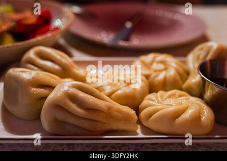 Piatto tradizionale georgiano khinkali servito su un piatto sotto una calda luce gialla. Gnocchi fatti in casa che mostrano autentica cucina e cultura georgiana. Foto Stock