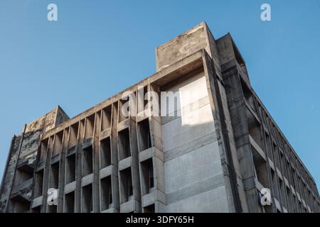 Una vista ad angolo basso di una massiccia facciata in cemento brutalista con un motivo geometrico ripetitivo di alette verticali e ombre profonde Foto Stock