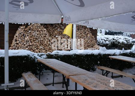 La neve ricopre il terreno mentre la legna da ardere è ordinatamente impilata dietro tavoli tranquilli. Kiev, Ucraina, Expocenter dell'Ucraina. 14 gennaio 2026. Foto Stock