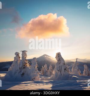 Winter mountains at sunrise with snowy peaks and warm colorful clouds. Scenic snowy landscape with bright morning light Foto Stock