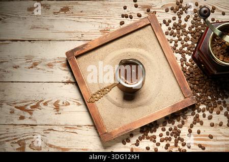 Caffè turco caldo in sabbia con macinacaffè e chicchi su fondo in legno Foto Stock