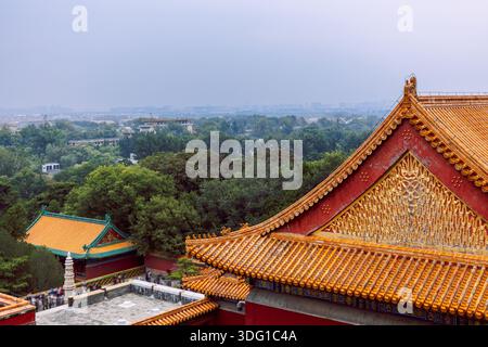 Palazzo d'Estate con motivi a rilievo dorato, tegole smaltate arancioni, superficie delle pareti rosse e paesaggio verde lontano sotto il cielo nebuloso, Pechino, Cina Foto Stock