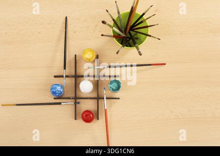 Vernici contenute in barattoli e pennelli in tazza verde sul tavolo di legno Foto Stock