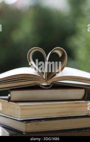 Pila di libri sul tavolo in giardino con uno aperto e pagine che formano la forma del cuore Foto Stock