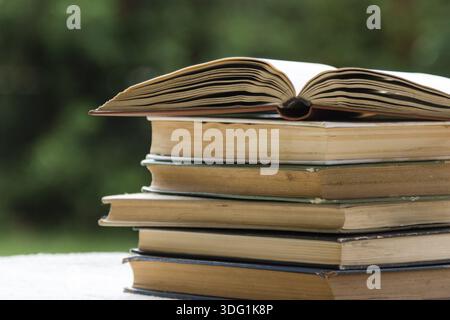 Una pila di libri sul tavolo in giardino con uno aperto Foto Stock