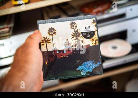 Parigi, Francia - 9 settembre 2025: Mano che tiene in mano un SACD sigillato Hotel California Eagles in un allestimento audiofilo con l'iconica copertina visibile vicino a un'area aperta Foto Stock