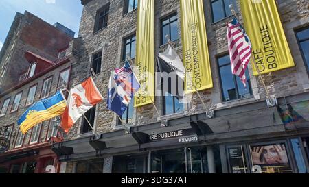 Montreal, QC, Canada - 7 agosto 2025: Edificio storico nella vecchia Montreal con varie bandiere battenti e striscioni per mostre d'arte contemporanea Foto Stock