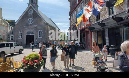 Montreal, QC, Canada - 7 agosto 2025: Turisti e gente del posto camminano su una vivace strada acciottolata nella città vecchia di Quebec City, Canada, con una chiesa storica A. Foto Stock