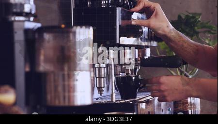 Estrazione del portafiltro, mani del barista con maniche arrotolate per preparare la tazza al caffè, con macchina per caffè espresso Foto Stock