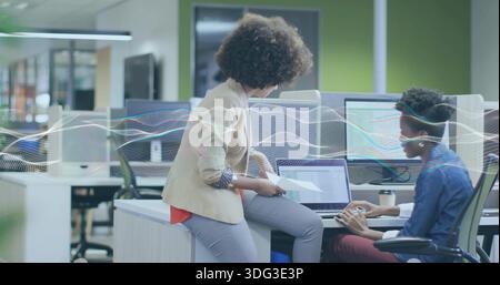 Collaborazione con due donne in giacca e camicia in denim che rivedono il laptop e le pagine stampate in ufficio Foto Stock