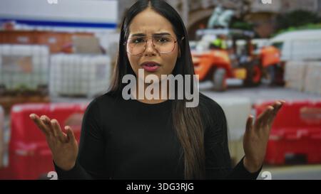 La donna diffonde le mani mostrando espressione frustrata in una scena di costruzione, mentre la giovane influencer latino ispanico esprime emozione in un si all'aperto Foto Stock