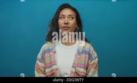 Il viso di una giovane donna guarda in studio sullo sfondo liscio di color verde acqua, indossando un cardigan a fantasia; scetticismo dubita della contemplazione. Foto Stock