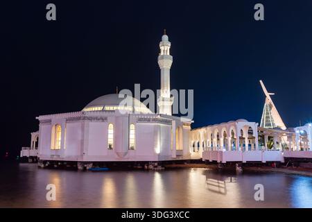 Jeddah, Arabia Saudita - 23 dicembre 2025: Moschea bianca illuminata di al Rahma, moschea galleggiante, si trova su acque calme, con un alto minareto e una curva Foto Stock