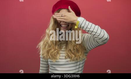 L'immagine di una donna che ricopre a mano lo studio mostra una giovane donna bionda in berretto e a righe con occhi sorridenti. Foto Stock