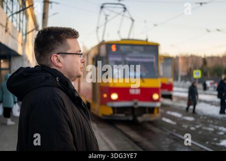 uomo ad una fermata del tram in russia, giovane in piedi alla fermata dell'autobus che aspetta il tram. traffico Foto Stock