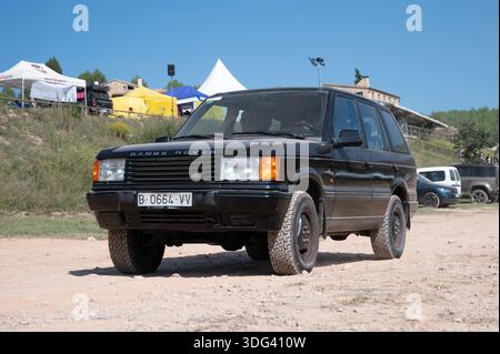 Vista frontale di un classico SUV di lusso Land Rover Range Rover P38A nero (modello 1995-2002) che guida su una pista fuoristrada polverosa sotto un cielo azzurro. Foto Stock