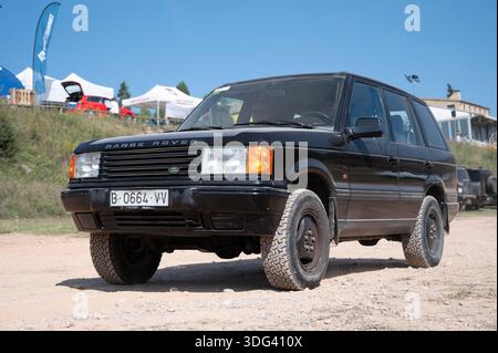 Vista frontale di un classico SUV di lusso Land Rover Range Rover P38A nero (modello 1995-2002) che guida su una pista fuoristrada polverosa sotto un cielo azzurro. Foto Stock