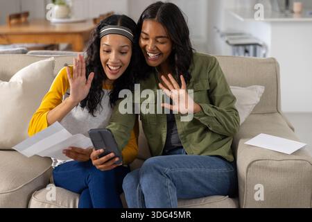 Mamma e figlia adolescente diverse che tengono in mano lo smartphone mentre mostrano un foglio di carta Foto Stock