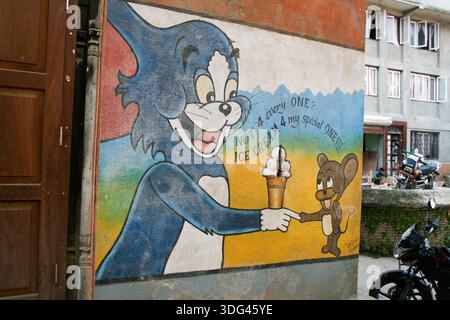 Murale dipinto su un muro raffigurante Tom & Jerry con il gatto che offre il gelato al topo. Patan, Durbar Square, Nepal. Foto Stock