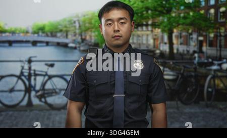 L'uomo si trova accanto al canale con un distintivo visibile sull'uniforme accanto alle biciclette parcheggiate vicino all'acqua in strada all'aperto; servizio. Foto Stock