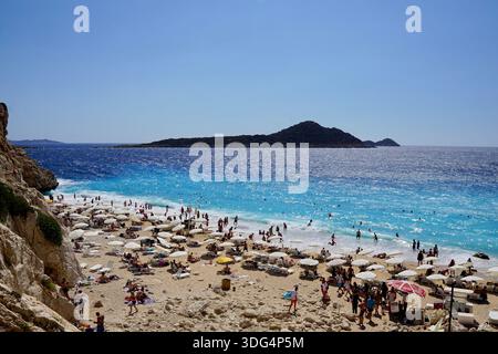 Affollata spiaggia di Kaputaş tra Kaş e Kalkan, Turchia, con acque turchesi del Mediterraneo, ombrelloni e nuotatori in una giornata estiva. Foto Stock