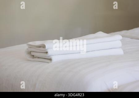 Una pila di asciugamani bianchi puliti piegati ordinatamente su un morbido letto in una comoda camera da letto che rappresenta il relax, l'ospitalità e la freschezza del bagno Foto Stock