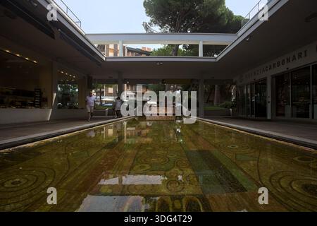 Milano Marittima, Italia - 22 SETTEMBRE 2025 - piscina e fontana con pavimento a mosaico in una piccola piazza delimitata dal portico di un edificio Foto Stock