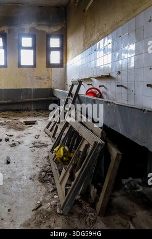 Interno di un bagno deteriorato in un edificio abbandonato, con lavabi rotti, telai delle finestre caduti e detriti sparsi. Foto Stock