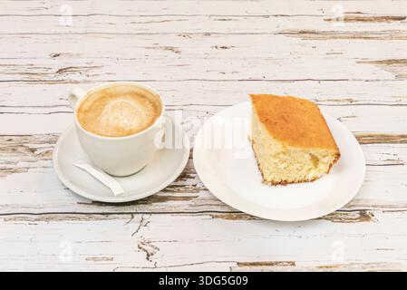 Un piacere semplice e quotidiano in primo piano: La superficie dorata e leggermente croccante di una torta di spugne alla vaniglia contrasta con il nero intenso del caffè in una ruggine Foto Stock
